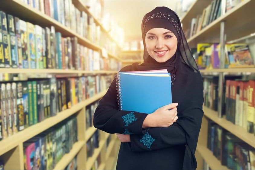 Arabischer Student steht mit Büchern im Arm in der Bibliothek.