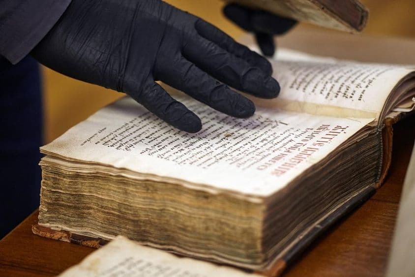 Der behandschuhte Bibliothekar hält ein seltenes Buch.