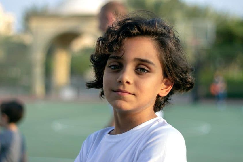 Ein niedlicher kleiner Junge steht auf einem Basketballfeld und lächelt.