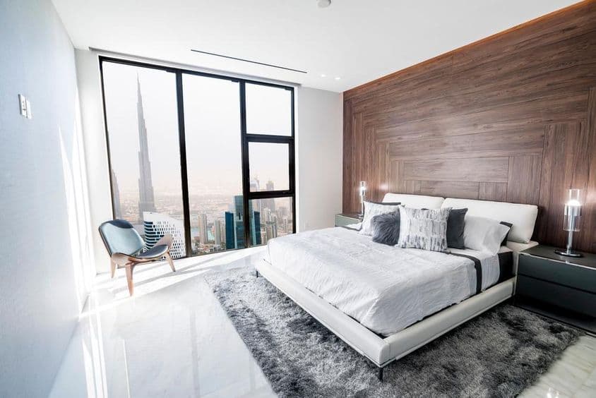 Luxuriöses Schlafzimmer mit weißer Decke und holzverkleidung, mit Blick auf die Innenstadt von Dubai.