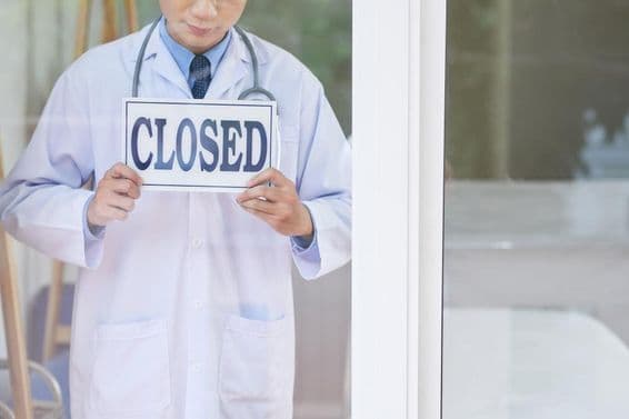 Ein Mann in medizinischer Uniform hält ein geschlossenes Schild.