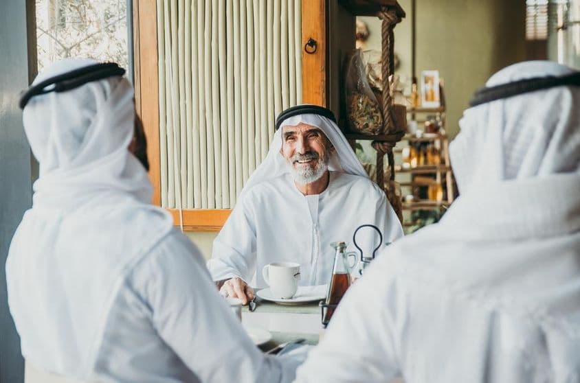 Drei Geschäftsleute genießen Tee in Dubai in traditioneller Emirati-Kleidung.