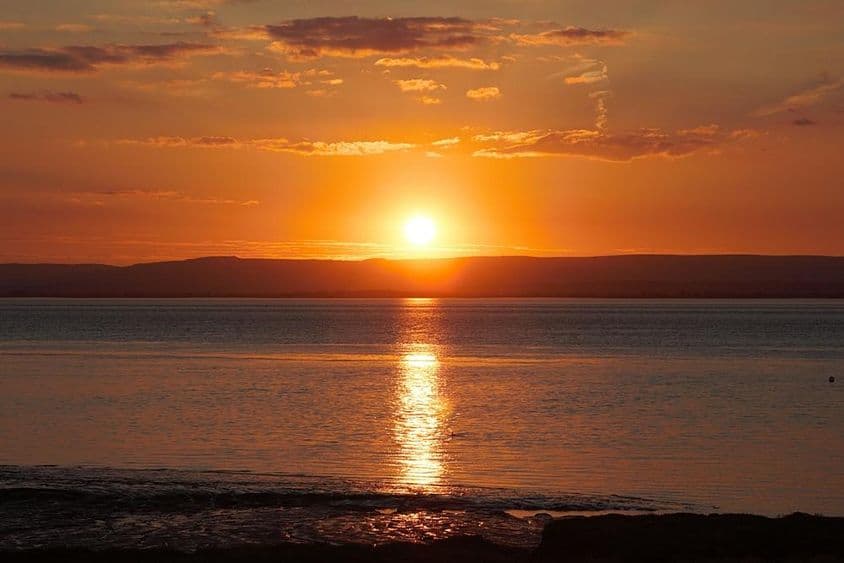 Sonnenuntergang, der sich während der Sommersonnenwende auf Wasser und Wolken spiegelt.