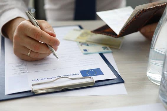 Ein Mann hält einen Reisepass und gibt persönliche Informationen in einen Schengen-Visumantrag ein.