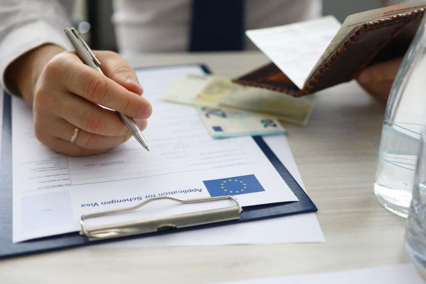 Ein Mann hält einen Reisepass und gibt persönliche Informationen in einen Schengen-Visumantrag ein.