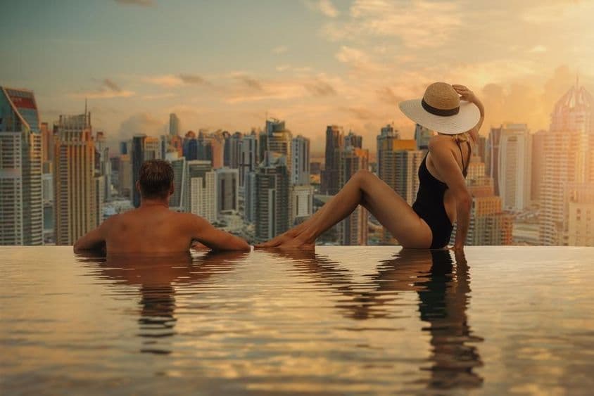 Ein Paar genießt Dubais Skyline mit Wolkenkratzerarchitektur vom Infinity-Pool bei Sonnenuntergang.