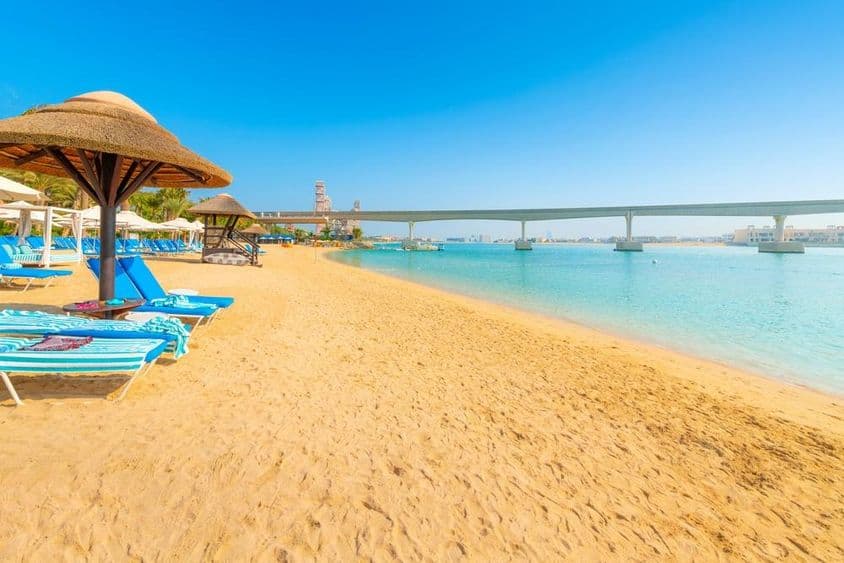 Auf einem Sandstrand des Arabischen Golfs überquert die Monorail der Palm Jumeirah Island das Meer in Dubai.