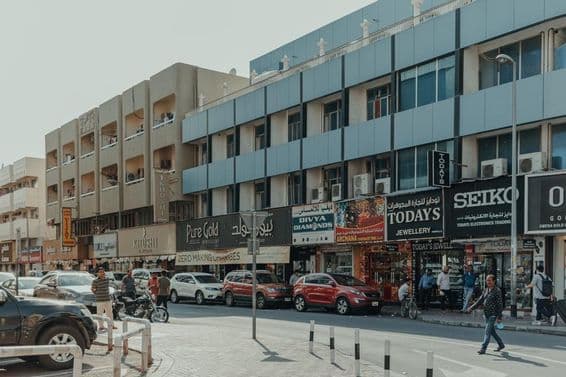 Belebte Straße in Bur Dubai mit Schmuckgeschäften, Fußgängern und Autos an einem sonnigen Tag.