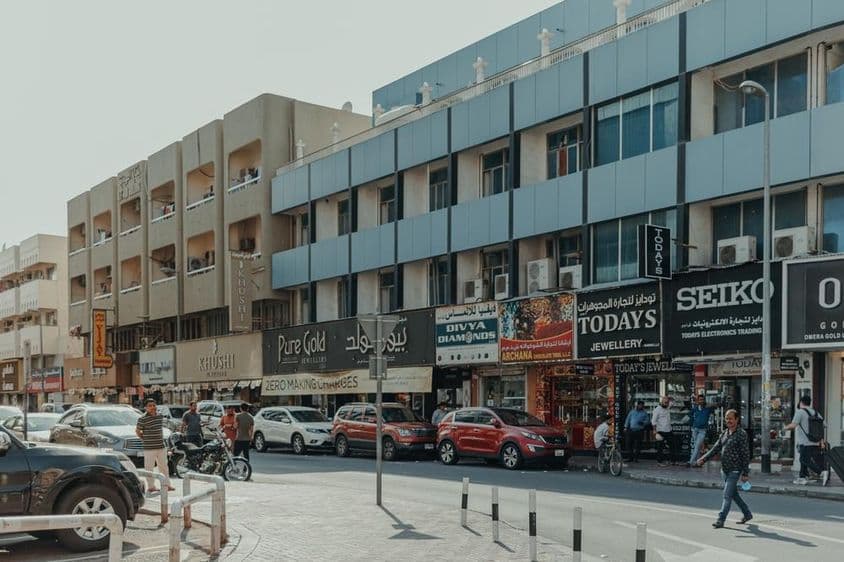 Belebte Straße in Bur Dubai mit Schmuckgeschäften, Fußgängern und Autos an einem sonnigen Tag.