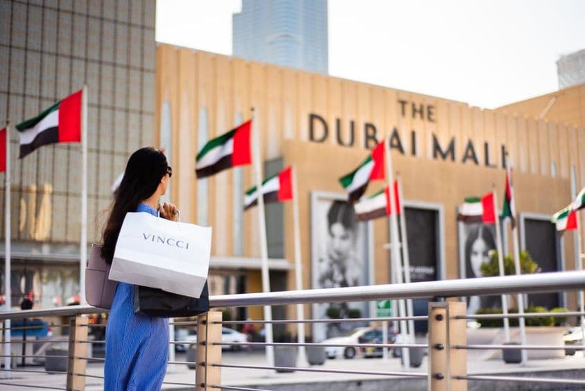 Asiatische Touristin mit Einkaufstaschen am Haupteingang der Dubai Mall.