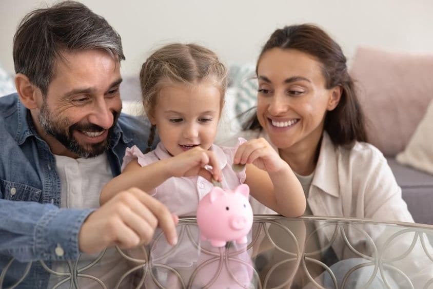 Glückliche Eltern lehren Tochter, Geld zu sparen.