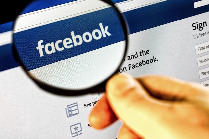 Facebook-Startseite auf einem Monitor durch eine Lupe betrachtet.