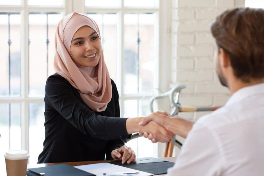 Arabische HR-Managerin im Hijab schüttelt einem männlichen Bewerber die Hand.