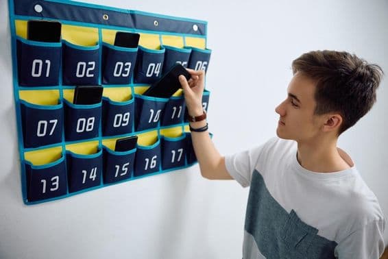 Schüler lässt Smartphone in einem an der Wand montierten Handy-Organizer.