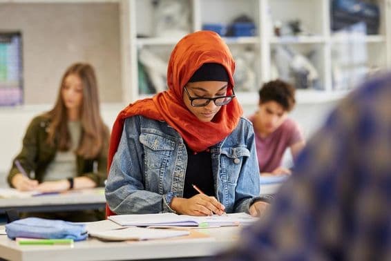 Junge Studentin in Hijab, die lernend Notizen macht.