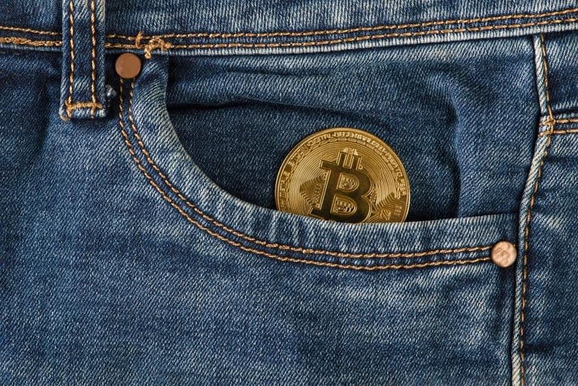 Eine goldene Bitcoin-Münze liegt in einer Jeanstasche.