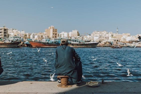 Mann genießt die Aussicht am Wasser mit Booten und Möwen am Dubai Creek.