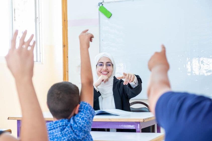 Schüler heben die Hände, um Anwesenheit zu signalisieren und dem Lehrer zu antworten.