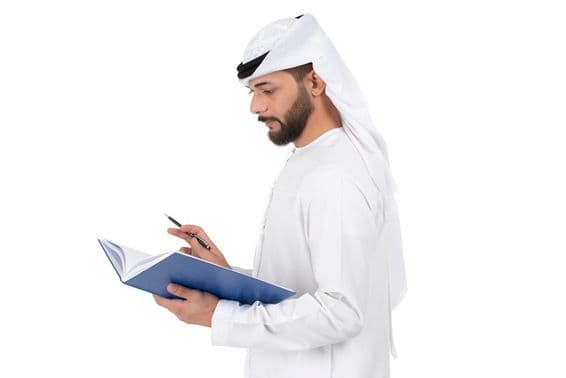 Junger arabischer Lehrer steht und schreibt im Buch.