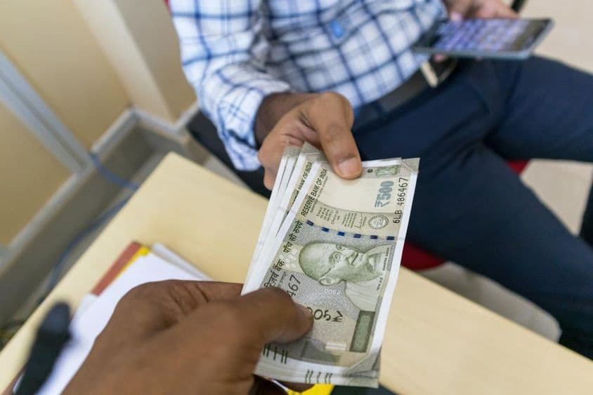 Eine Person überreicht einer anderen Person einen indischen 500-Rupien-Geldschein.