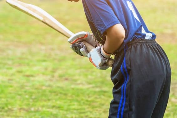 Asiatische junge Cricketspielerin in Schutzkleidung schlägt mit einem Schläger einen Ball auf dem Spielfeld.