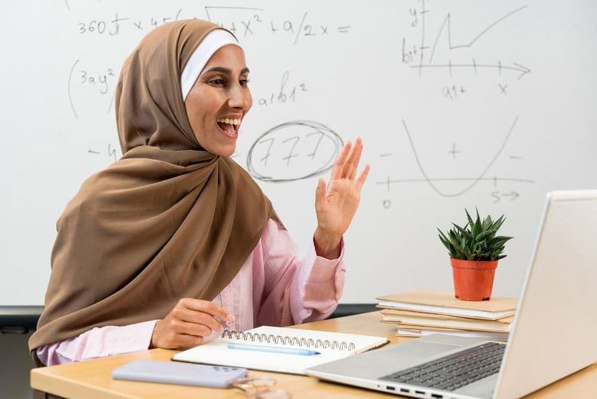 Weibliche Lehrerin im Hijab winkt Studenten während eines Online-Kurses zu.