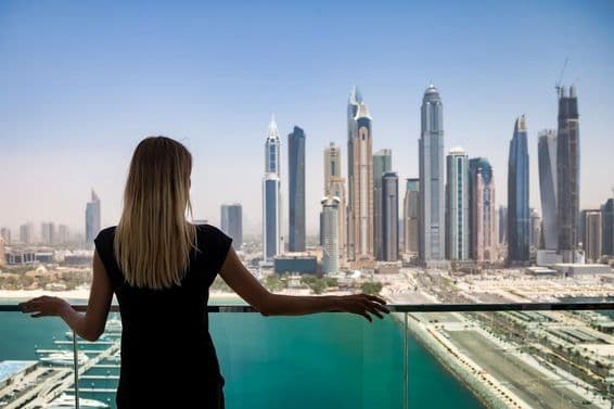 Eine nachdenkliche Frau in Schwarz auf einem Balkon mit Blick auf die Wolkenkratzer von Dubai, Vereinigte Arabische Emirate.
