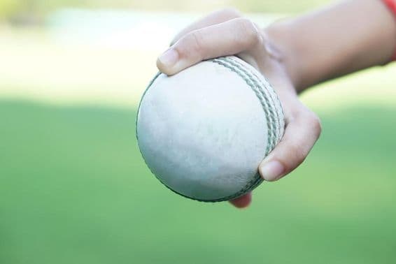 Ein Cricketspieler hält einen weißen Leder-Cricketball.
