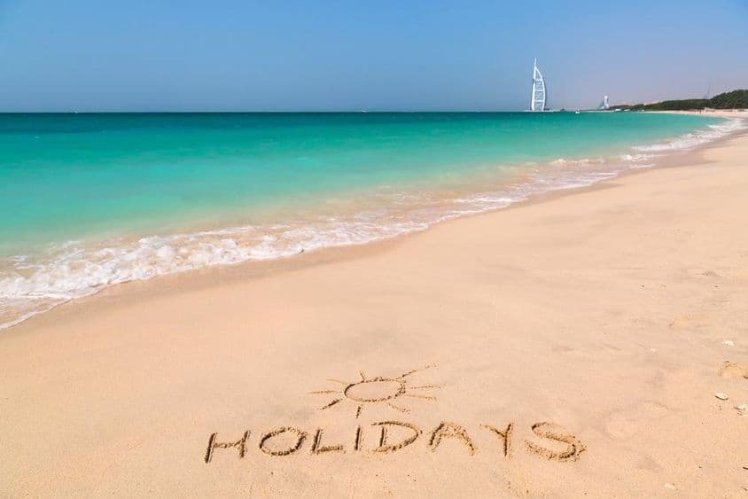 Urlaubsschild an einem Strand mit türkisfarbenem Wasser.