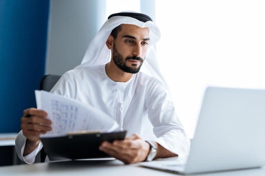 Mann arbeitet mit einem Laptop im Büro in Dubai, gekleidet in traditioneller weißer Emirati-Kleidung.