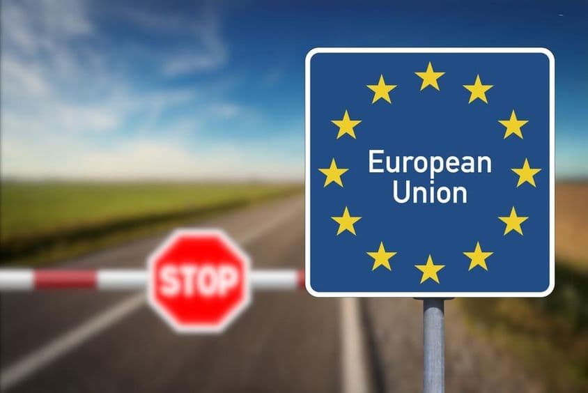 Emblem der Europäischen Union und ein Grenzübergang mit Schranke und Stoppschild.