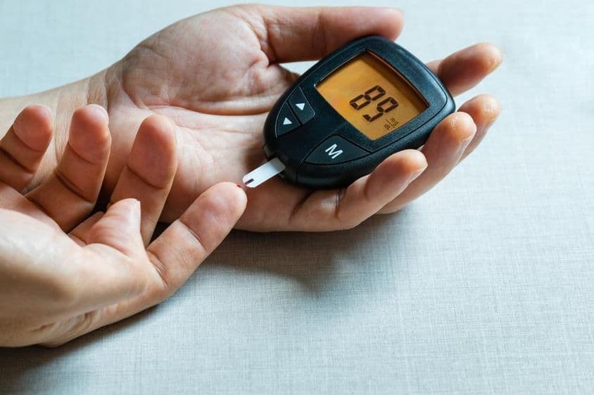 Die Hände eines Mannes nutzen ein digitales Blutzuckermessgerät zur Überwachung von Diabetes.