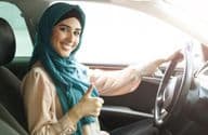 Glückliche arabische Frau im Hijab fährt ihr Auto mit einem Daumen hoch.