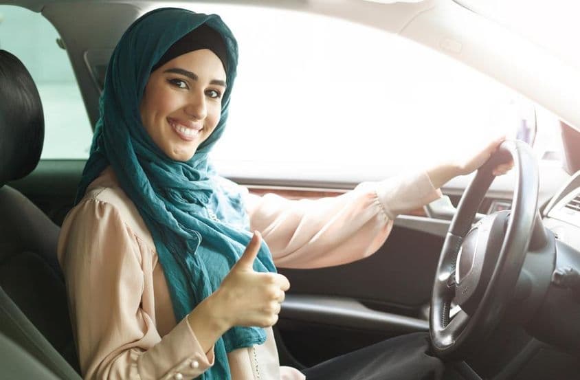 Glückliche arabische Frau im Hijab fährt ihr Auto mit einem Daumen hoch.