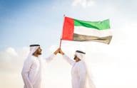 Arabische Männer in Kanduras, die in der Wüste gehen und eine Flagge halten.