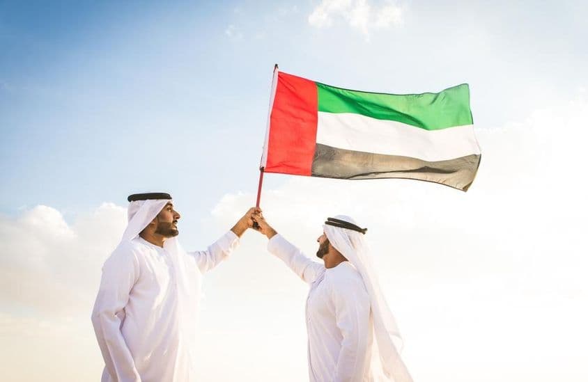 Arabische Männer in Kanduras, die in der Wüste gehen und eine Flagge halten.