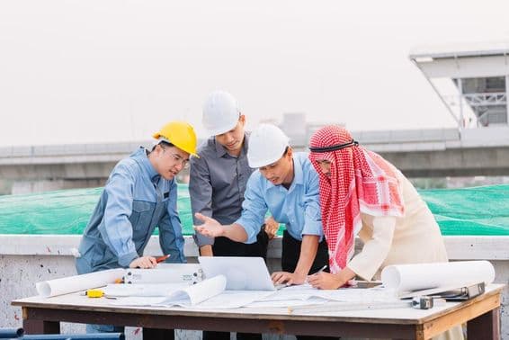 Arabischer Geschäftsmann, Ingenieur und Arbeiter mit Bauplänen, die einen Laptop nutzen.