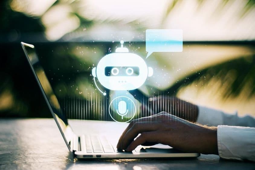 Eine Person tippt auf einem Laptop mit einem unscharfen Outdoor-Hintergrund, der ein Chatbot-Symbol zeigt.