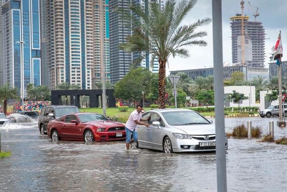 Menschen schieben Autos aus dem Wasser in überfluteten Straßen von Dubai.