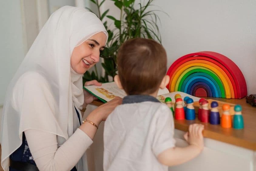 Eine muslimische Lehrerin und ein Kindergartenkind spielen mit bunten Spielzeugen.