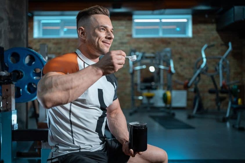 Muskulöser Bodybuilder mit perfektem Körper, der Protein im Fitnessstudio hält.