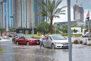 Menschen schieben Autos aus überfluteten Straßen in Dubai.