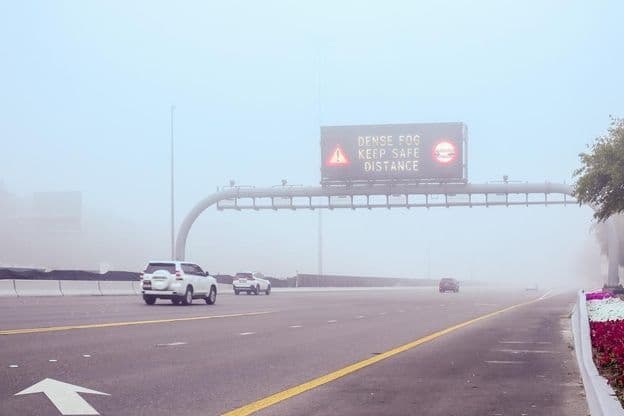 Nebel auf der Straße mit einem Schild 'Abstand halten'.