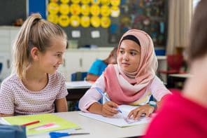 Muslimische Schülerin sitzt neben einem Klassenkameraden während einer Unterrichtsstunde.
