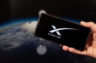 Eine männliche Hand hält ein Smartphone mit dem Starlink-Logo in seiner rechten Hand.