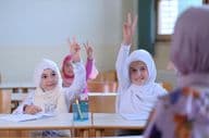 Muslimische Schulkinder heben die Hand, um die Fragen des Lehrers zu beantworten.