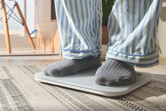Mann in gestreiften Pyjamas steht auf einer weißen digitalen Waage