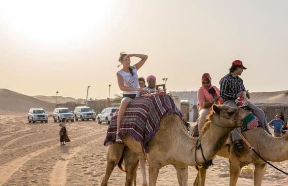 Touristen, die im Dubai-Wüstensand auf Kamelen reiten