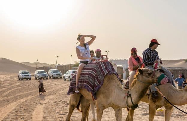 Touristen, die im Dubai-Wüstensand auf Kamelen reiten