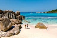 Zwei Reisende gehen am weichen weißen Sandstrand von Anse Cocos Beach auf den Seychellen spazieren.
